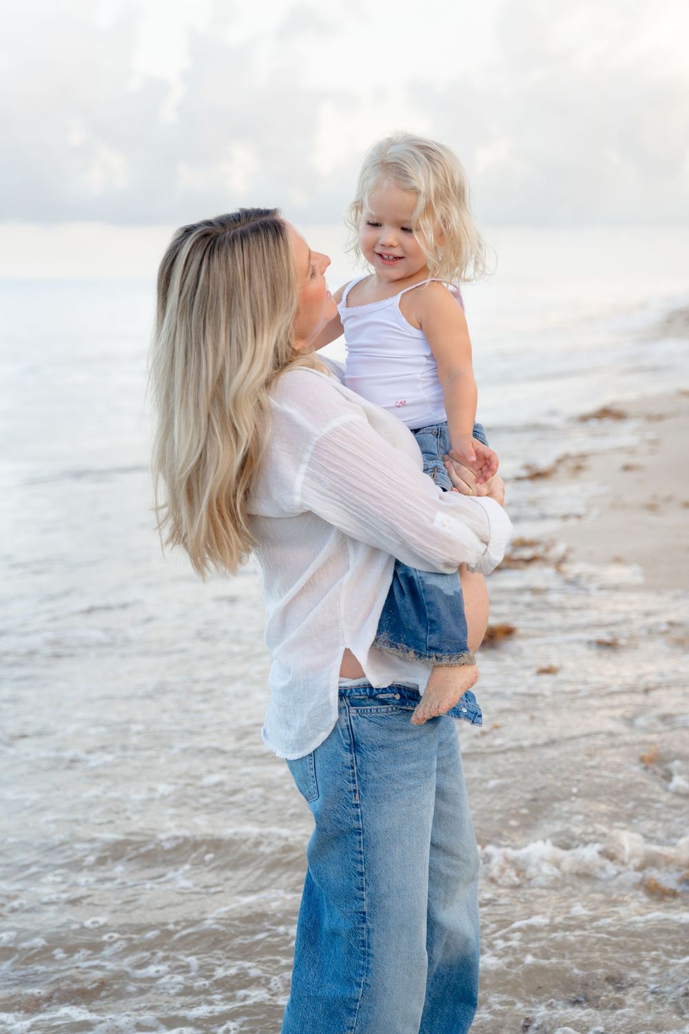 A tender moment shared between parent and child as they embrace playfully at the beach alongside rolling waves.