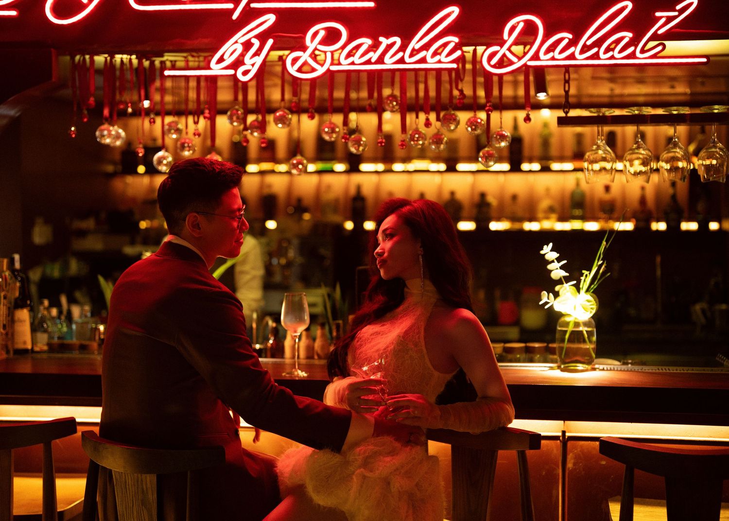 Couple sharing romantic moment at a warmly lit bar under a glowing neon sign.