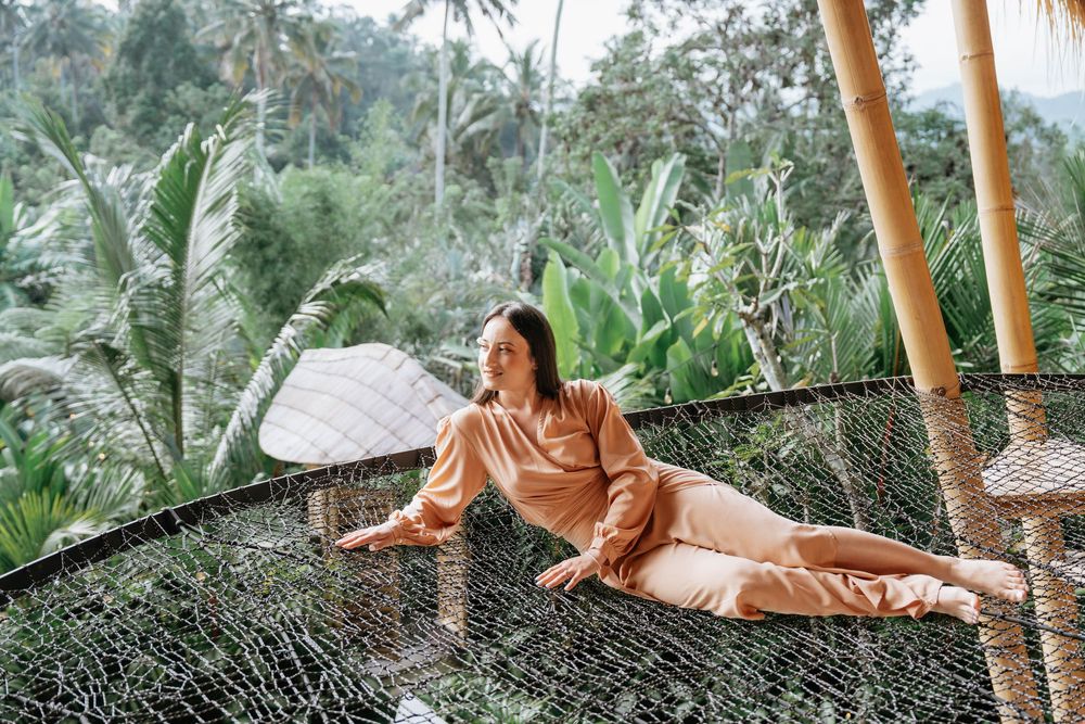 Person lounges on hammock in peaceful tropical garden setting with palm trees.