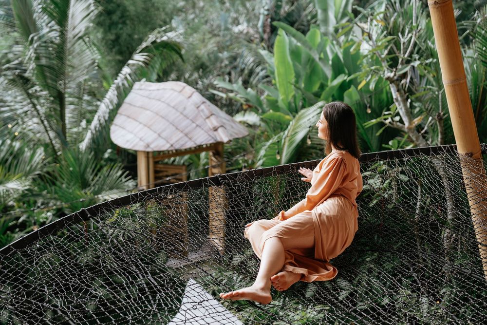 Person relaxes on hammock surrounded by tropical palm trees and lush vegetation.