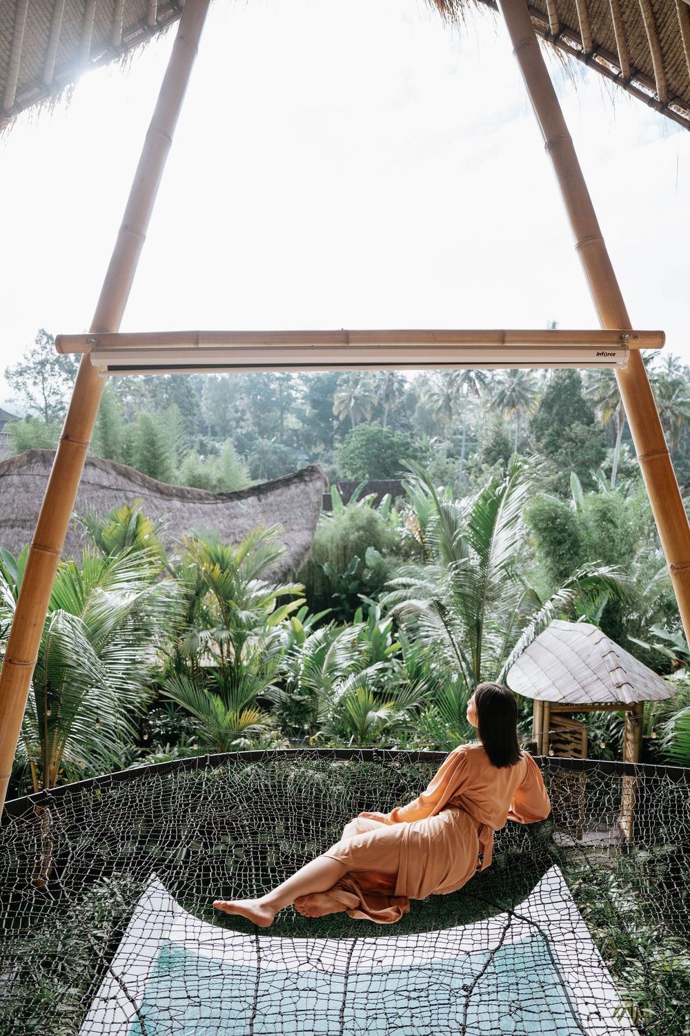 Person lounging in a net hammock surrounded by lush tropical foliage and palm trees.