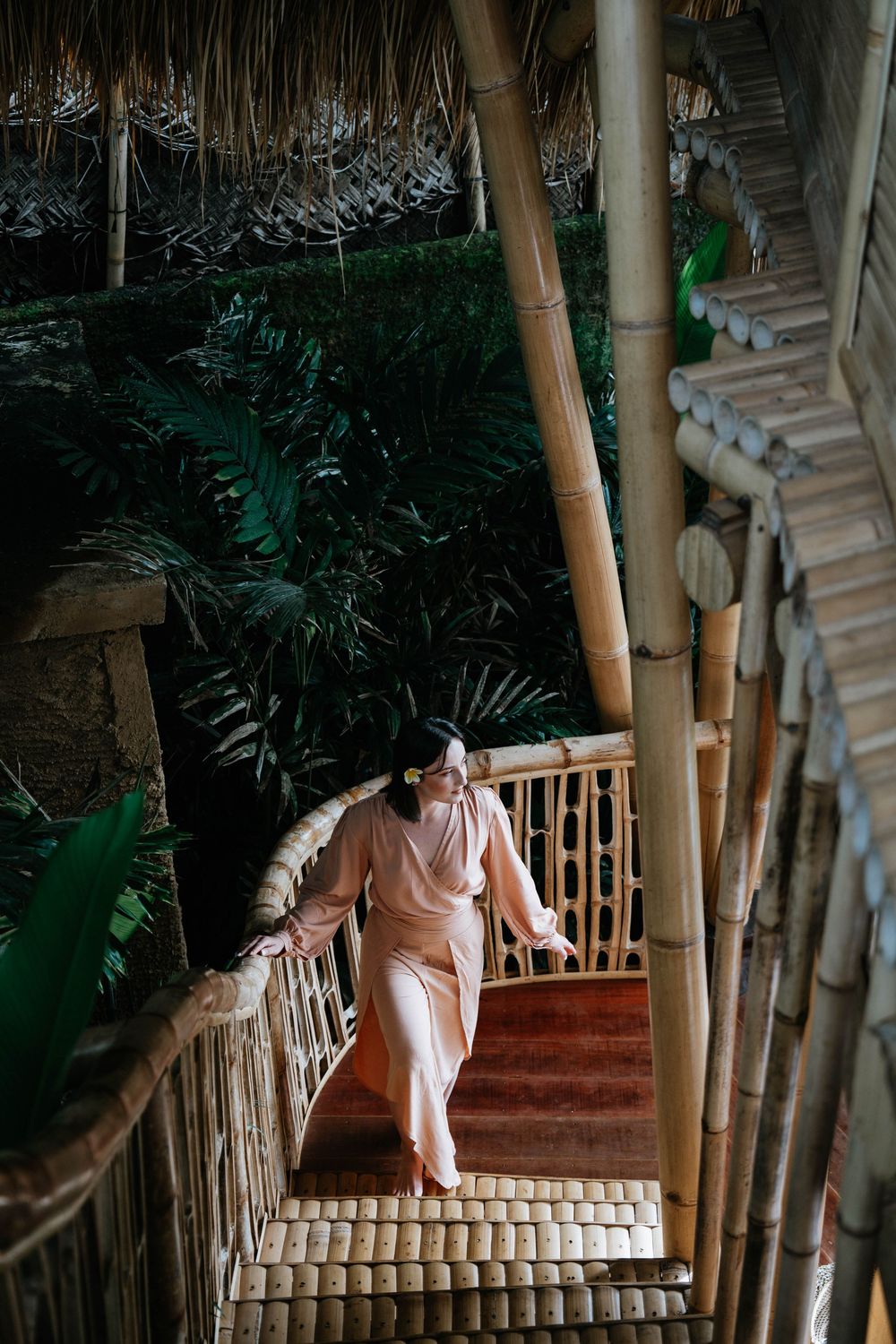 Person in peach outfit descending bamboo stairs in tropical setting.