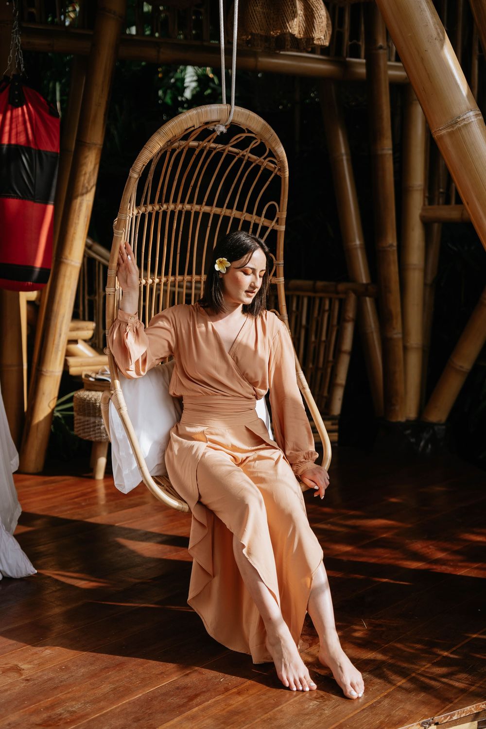 Person in peach dress sitting on rattan swing in bamboo interior.