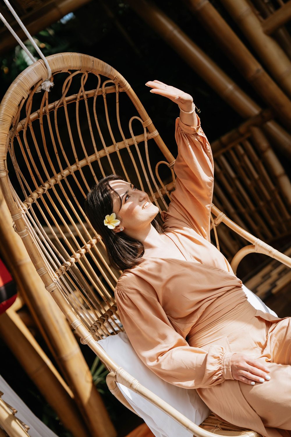 Woman in peach-colored dress lounging on bamboo furniture in tropical setting.