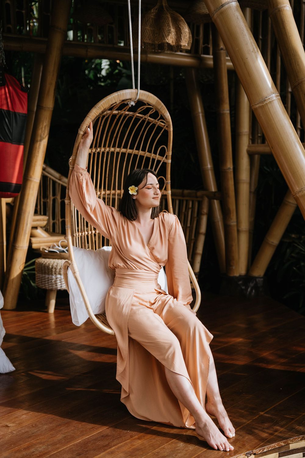 Bamboo interior with hanging rattan chair and person in flowing peach dress.