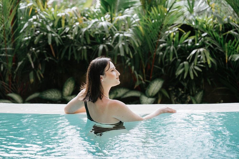 Person relaxing in infinity pool with tropical garden backdrop.