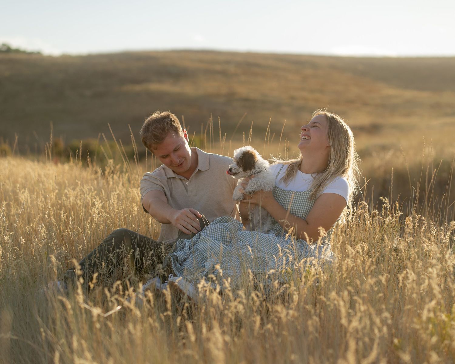 Joyful engagement photo of a couple in a sunlit field in Logan, Utah.