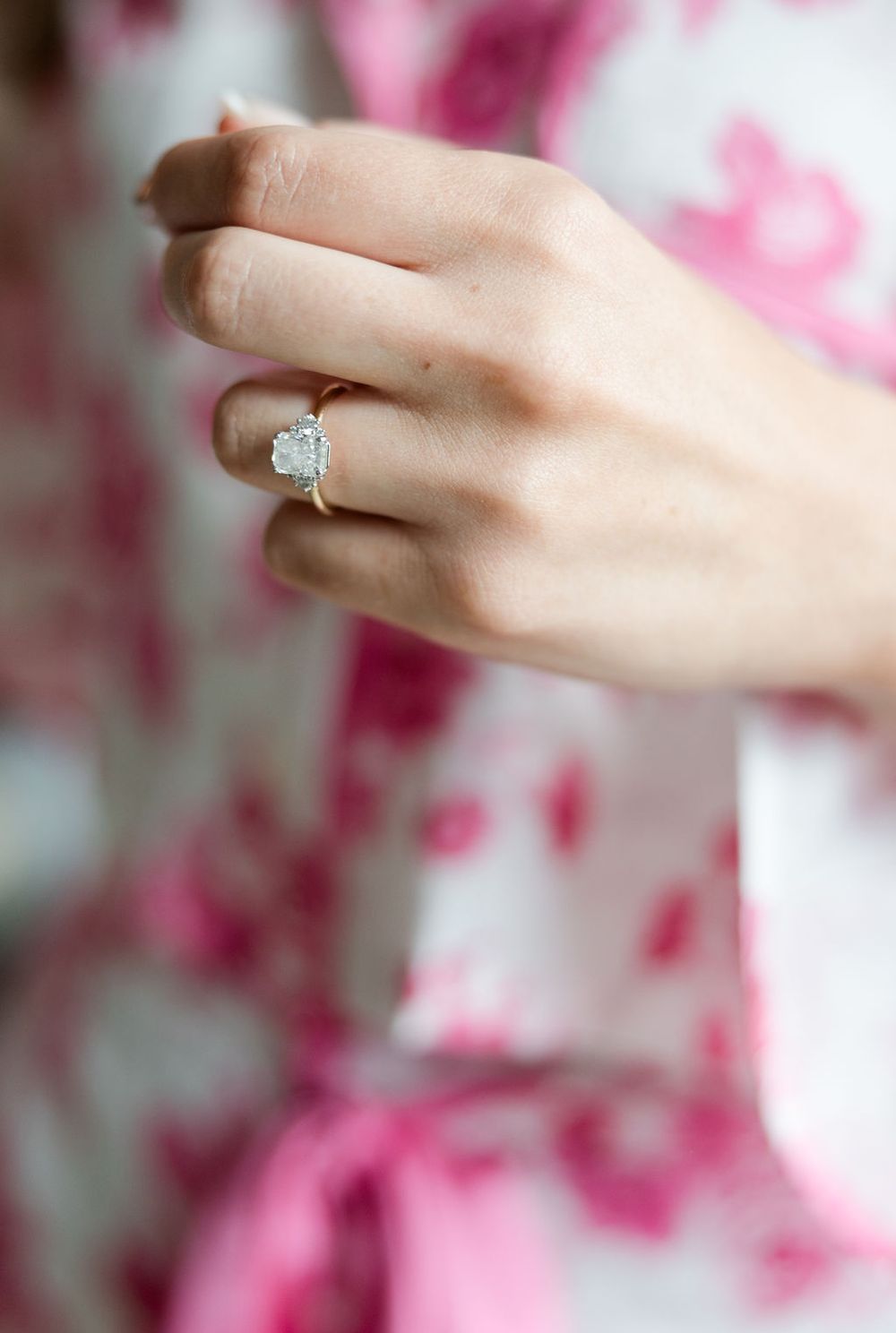 Close-up shots of an engagement ring on a hand against a pink floral background.