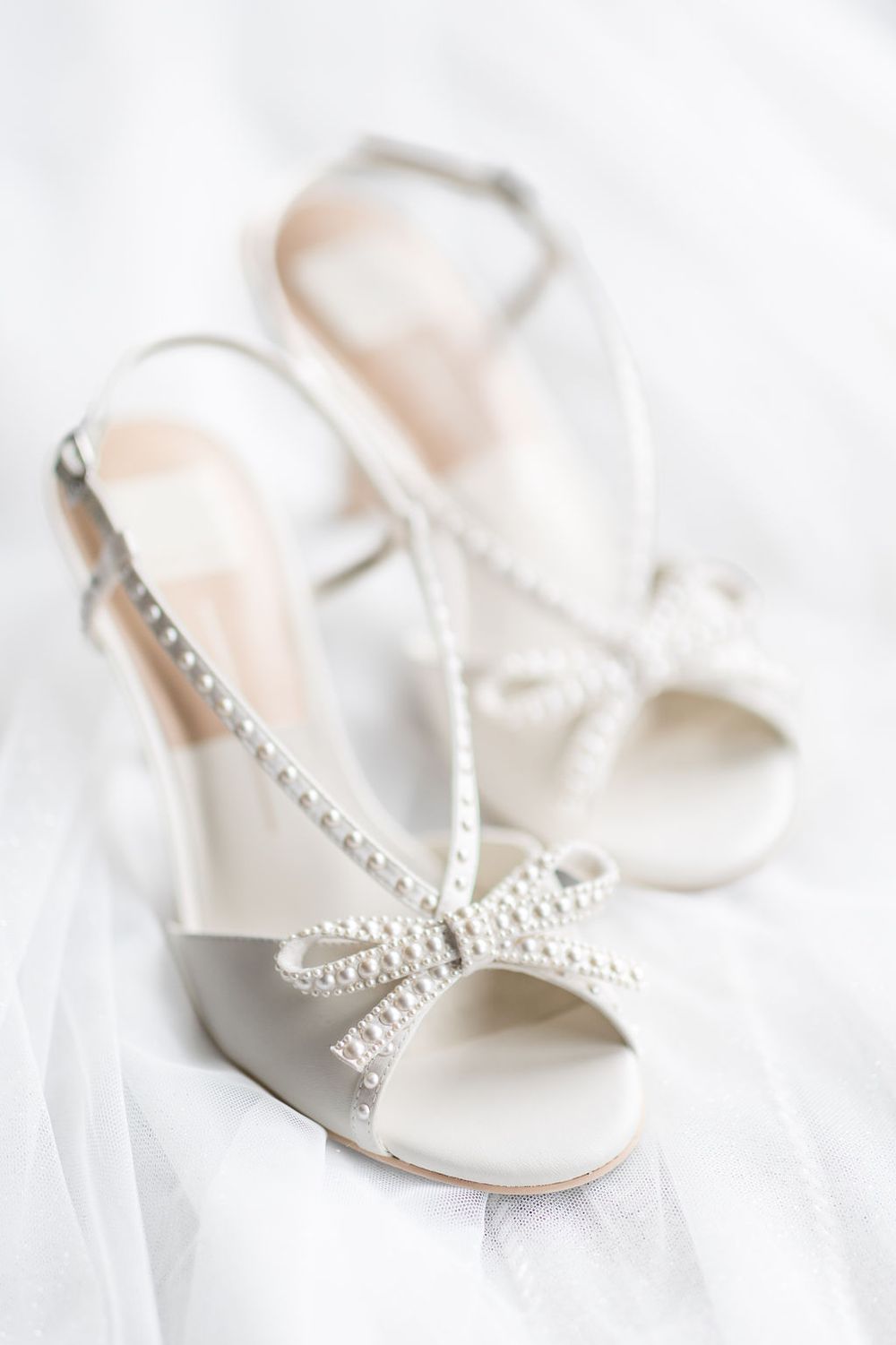 White bridal shoes with delicate pearl embellishments on a soft white background.