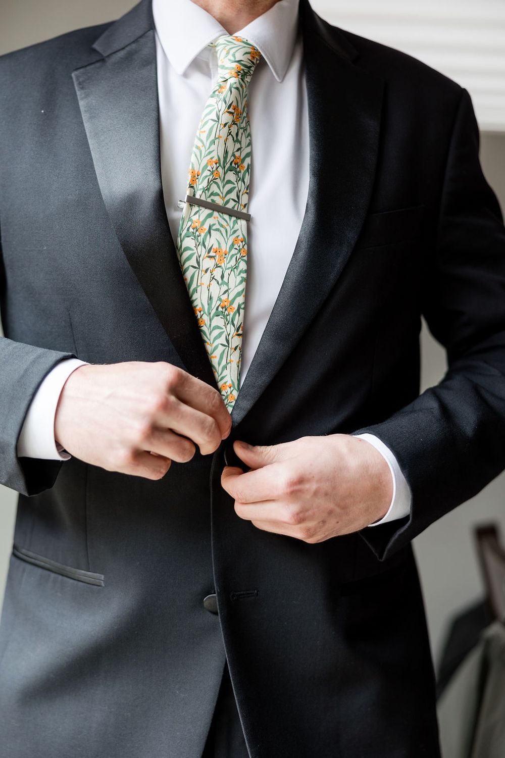 Detail shots of a groom's formal black suit and floral patterned tie.