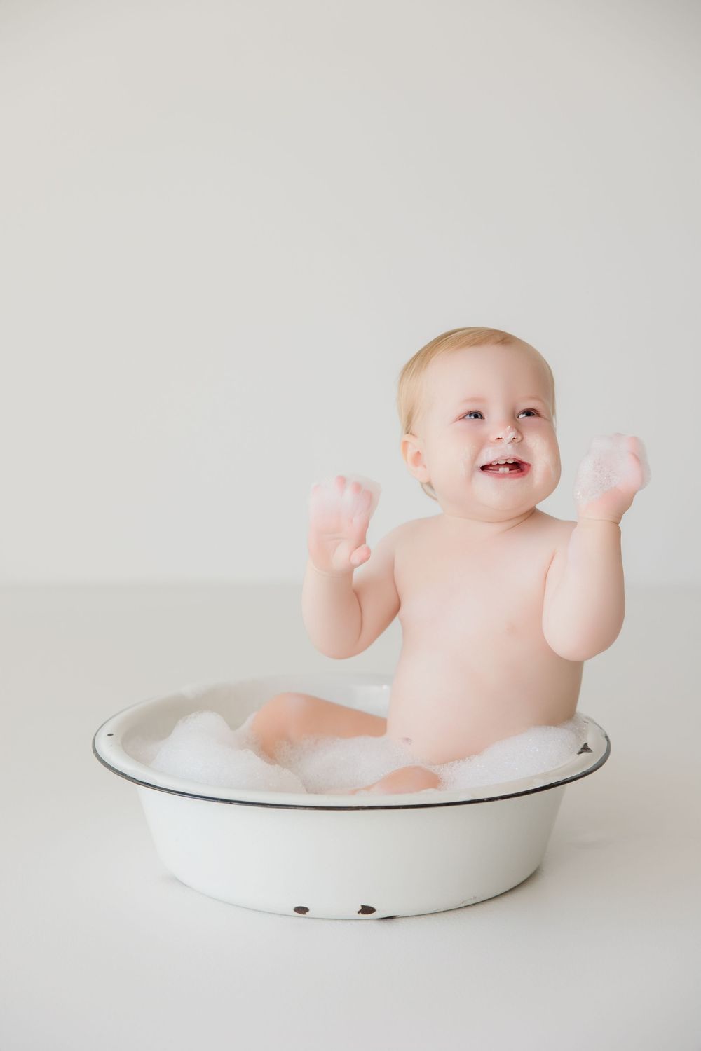 Happy baby playing and laughing while sitting in vintage white enamel basin.