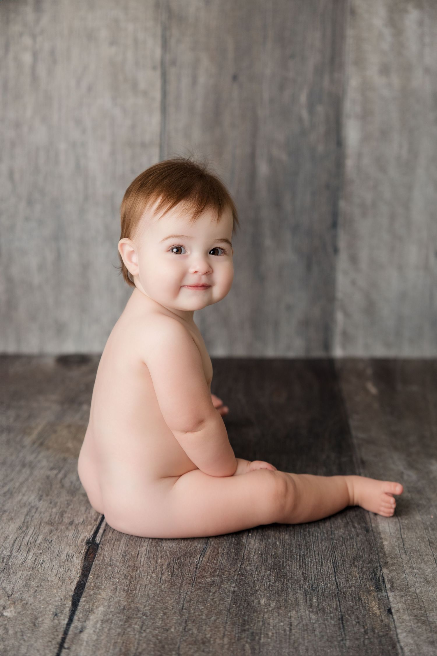 Series of five black and white artistic photos showing a baby lying on rustic wooden flooring.