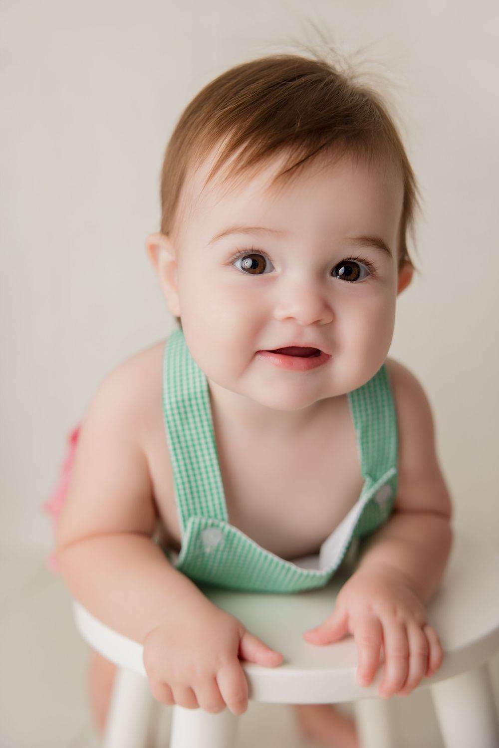 Baby wearing mint green gingham outfit smiles while sitting during portrait photography session.