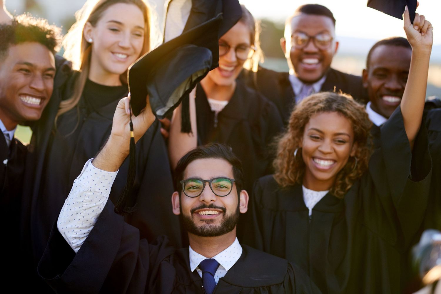 A group of graduates wearing black caps and gowns smile together during their commencement ceremony.