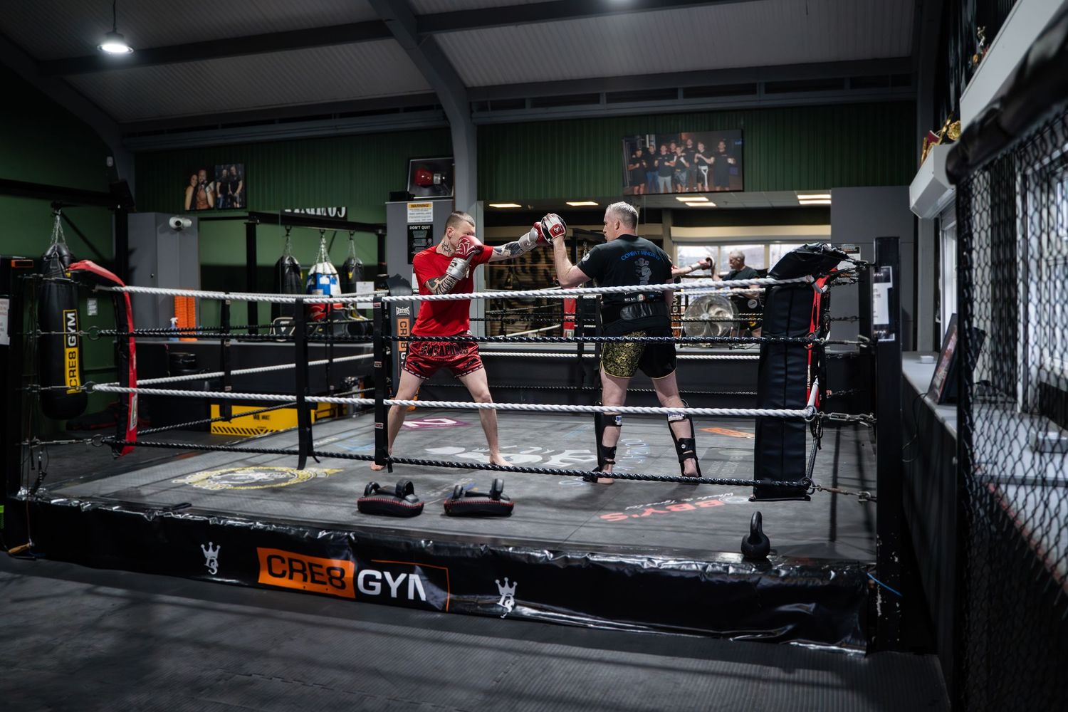 Wide angle view of an empty boxing gym with training equipment and ring.