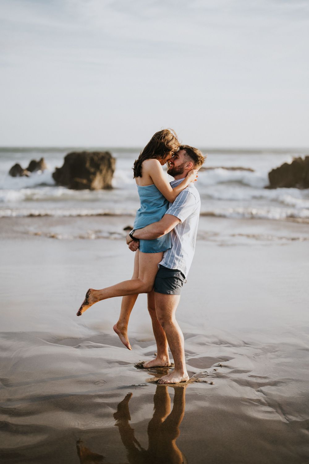 A playful couple lifts each other up while splashing in the ocean waves at sunset.