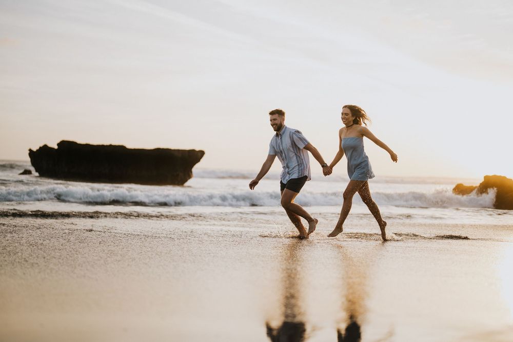 Two people run and play together on a scenic beach at sunset.