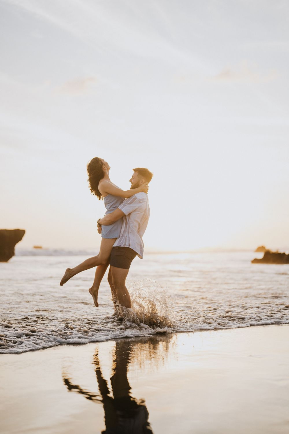 A couple splashes in the ocean waves during sunset creating dramatic silhouettes and water reflections.