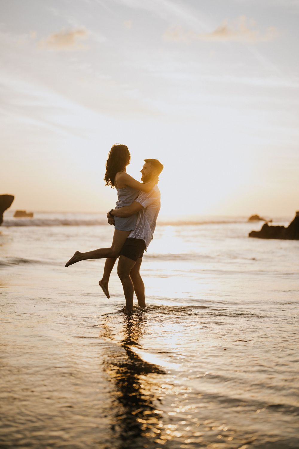 Two silhouettes dance in the shallow ocean water during a golden sunset.