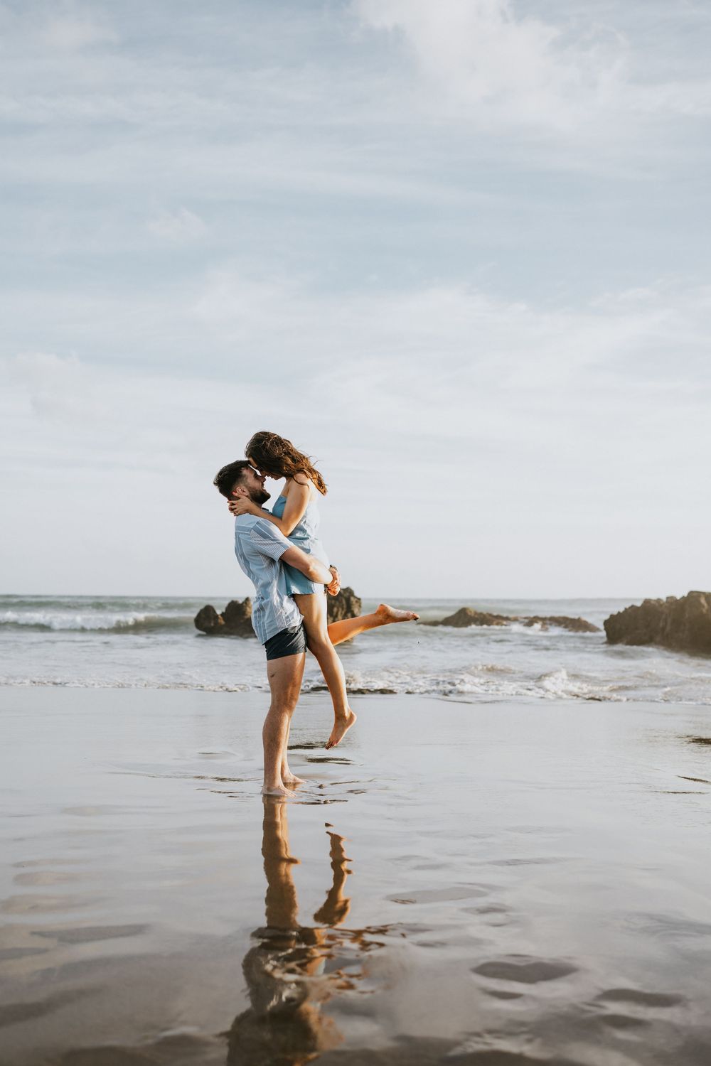 Romantic couple embracing and lifting each other on a misty beach shore.