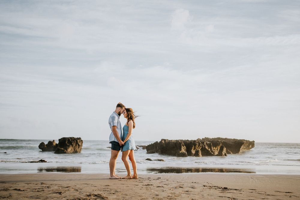 Two people walking along a scenic beach with rocky outcrops in the distance.
