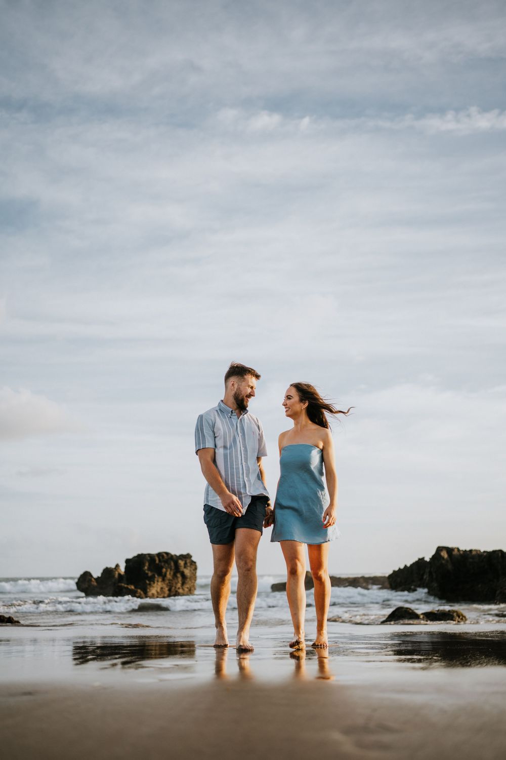 Two people enjoying a romantic moment on a cloudy beach with waves crashing nearby.