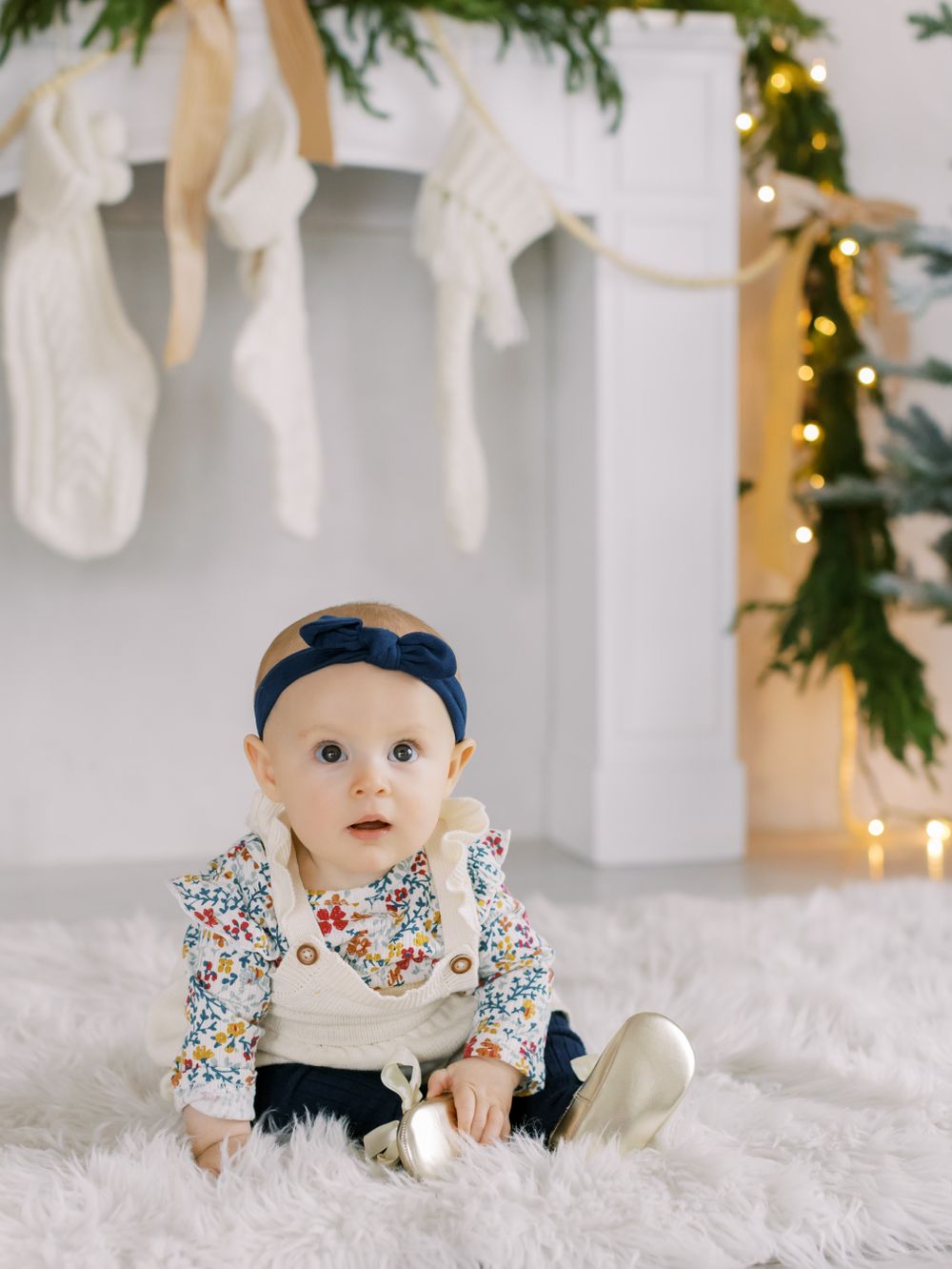 Baby at mantle with white and gold Christmas decorations fresh garland at White Space Studios