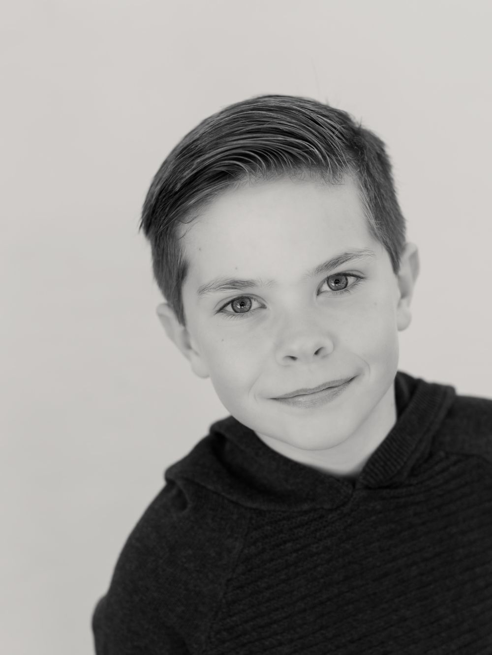 A close-up portrait of young person in black hoodie against light grey background.
