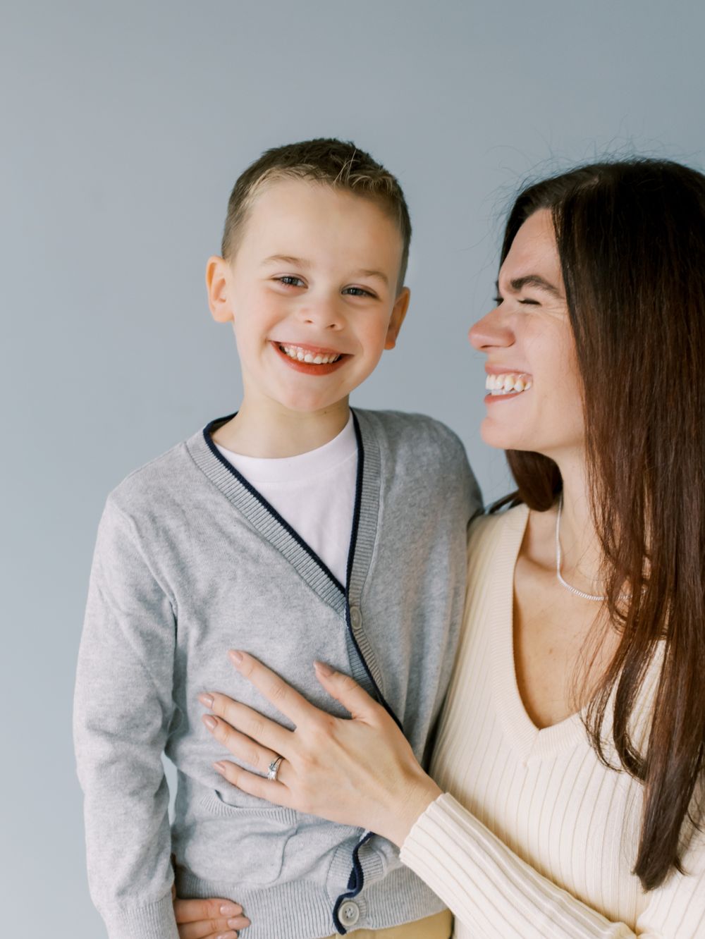 A tender moment captured between parent and child sharing laughter against grey backdrop.