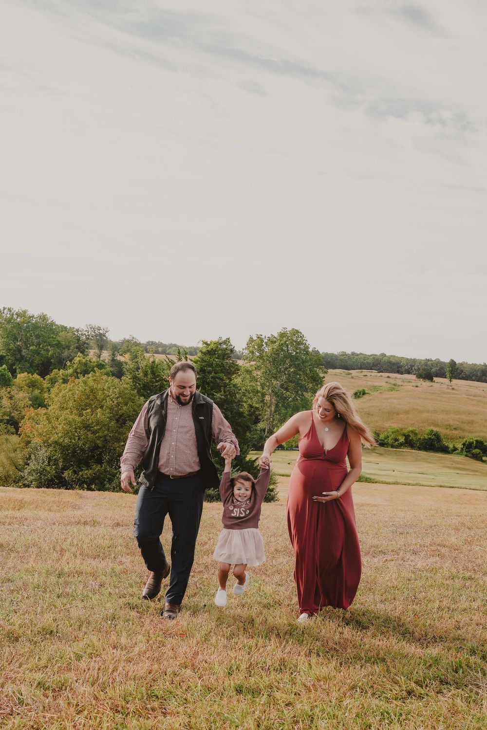Three people run joyfully through a sunlit meadow on a warm autumn day, creating a playful outdoor scene. Manassas, Virginia