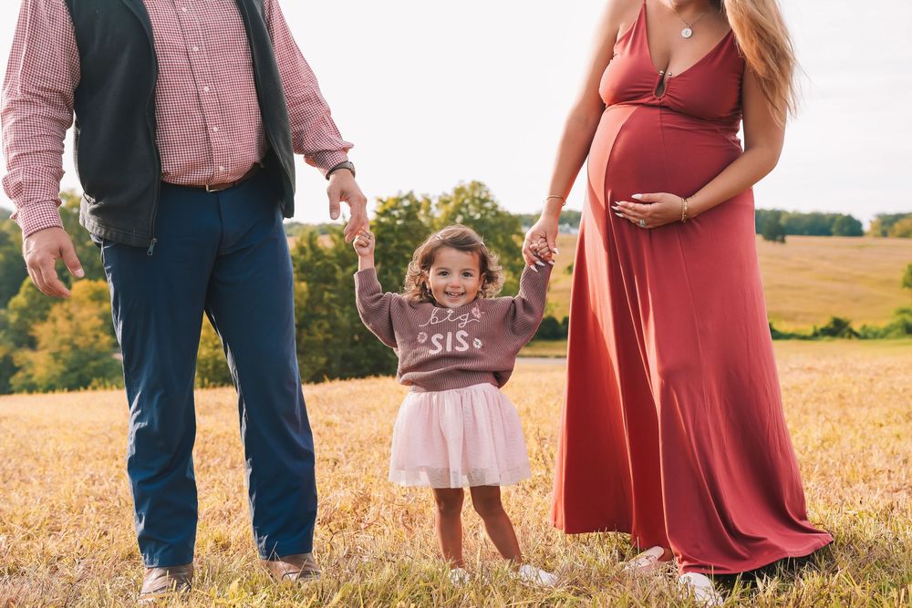 Family in coordinating red and pink outfits walking together in a golden wheat field at sunset.