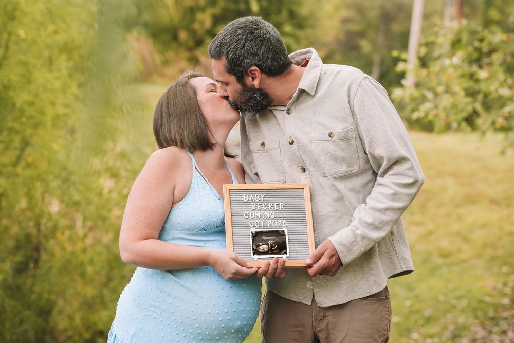 A couple in a garden setting holds a small chalkboard sign while embracing in soft natural light. Leesburg, Virginia