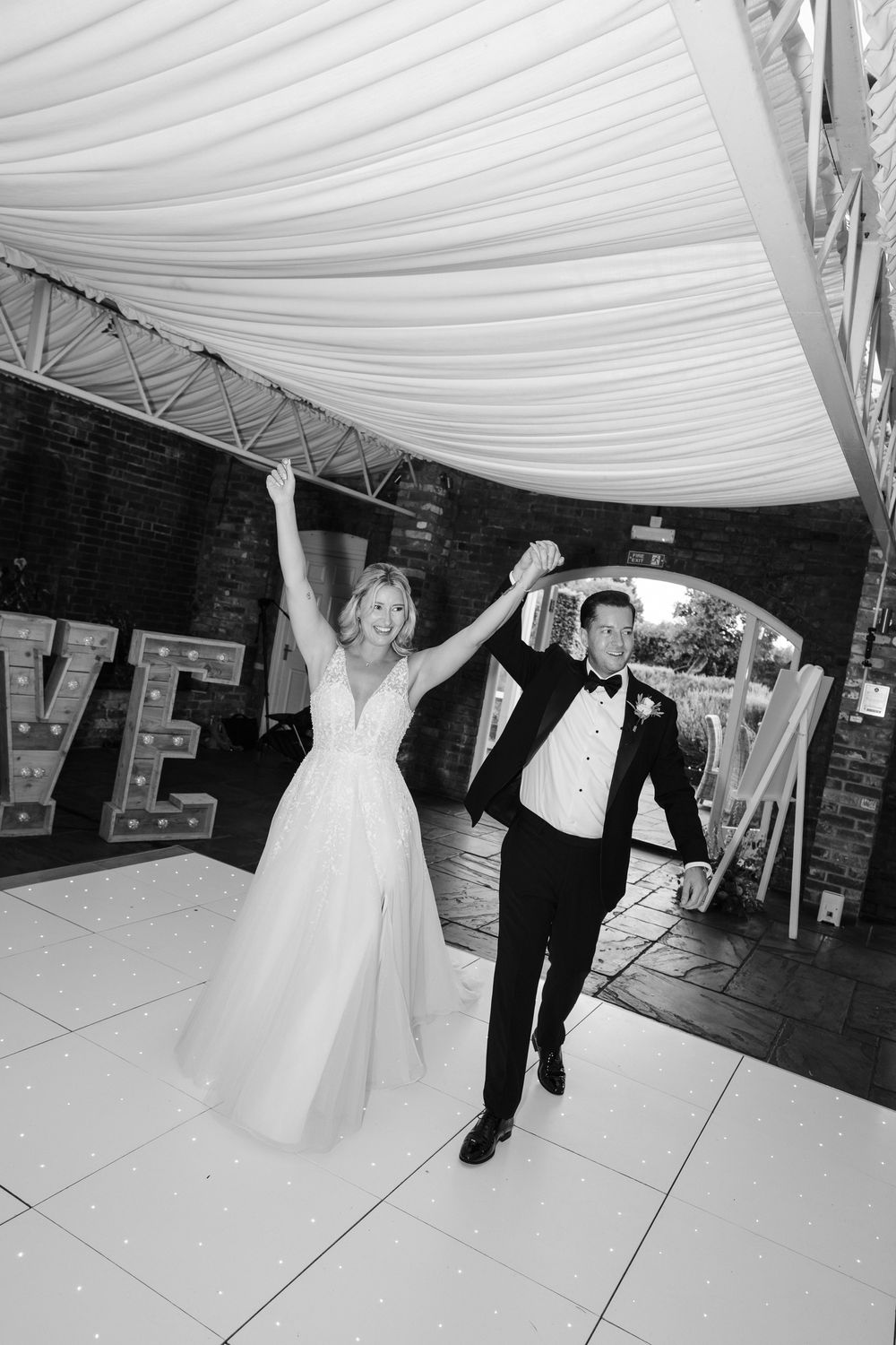 A couple celebrates on the dance floor under a white draped tent ceiling at an indoor wedding reception venue.