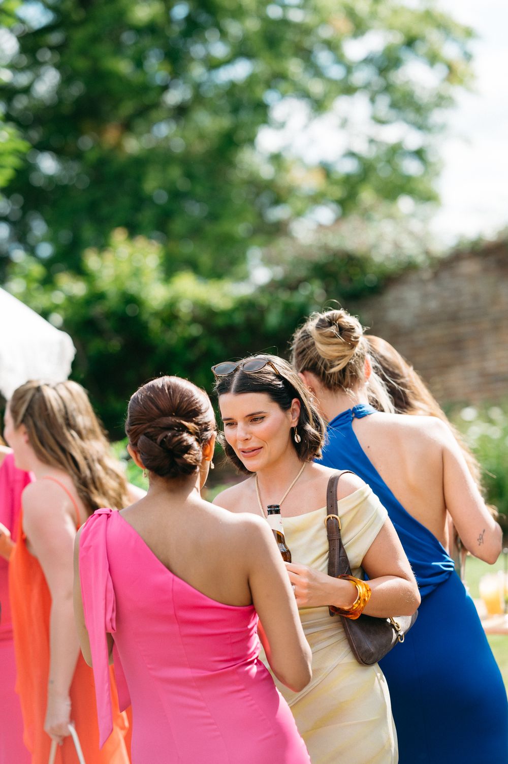 Line of bridesmaids in colorful dresses walking together outdoors at a summer wedding.
