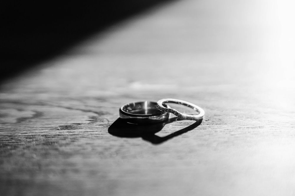 A close-up black and white photograph of wedding rings casting shadows on a textured surface.