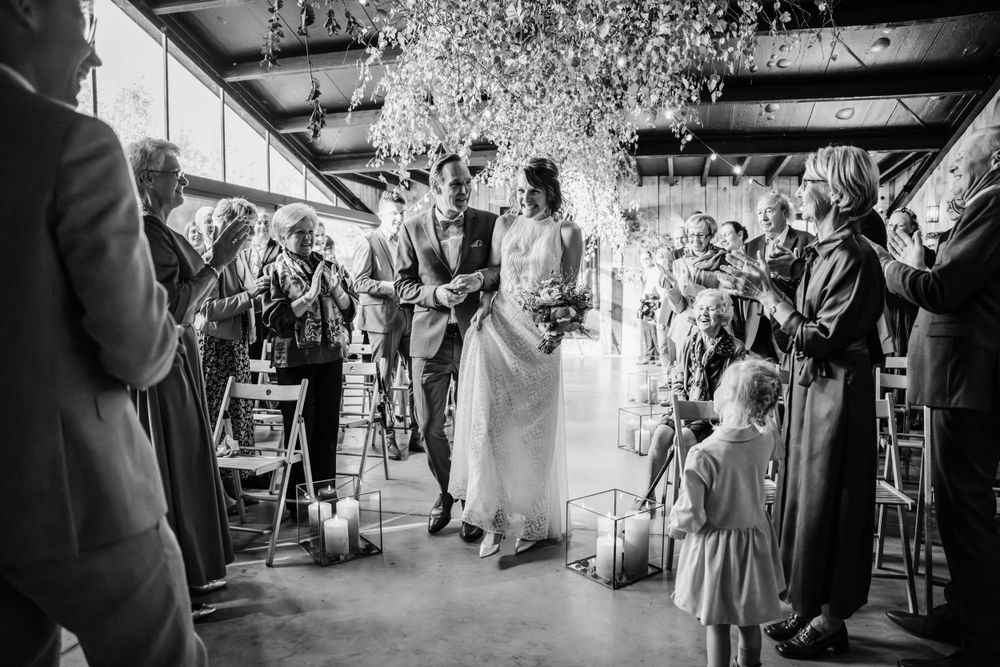 A joyful wedding celebration captured in black and white as guests toss confetti over a couple in a rustic venue.
