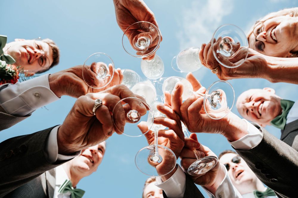 Low angle view of hands holding beer bottles in a celebratory circle against blue sky.