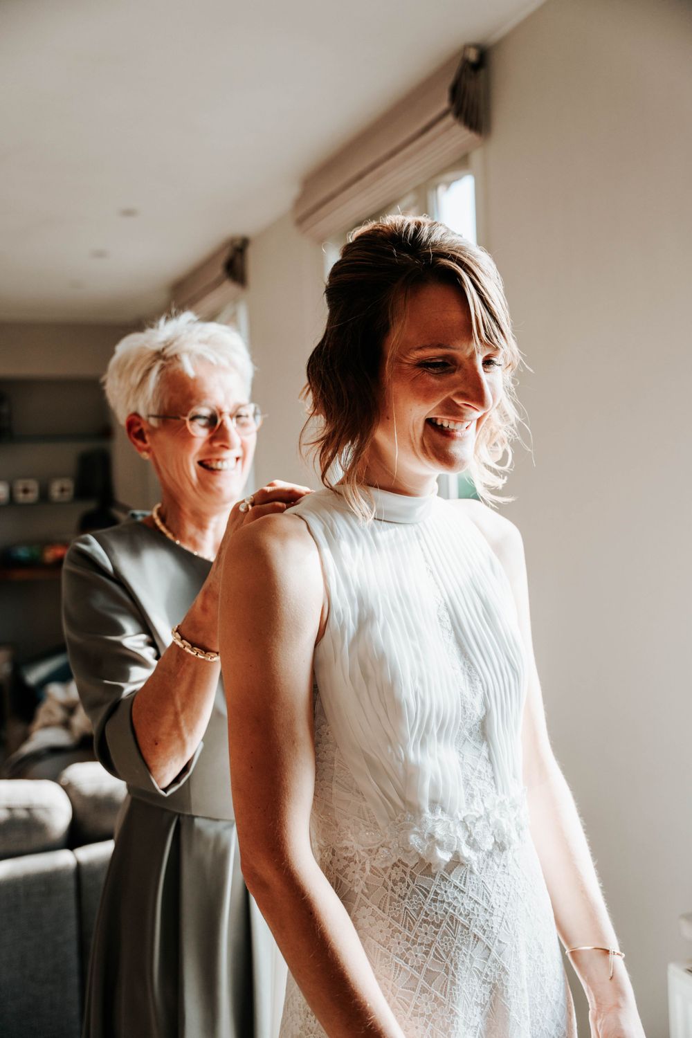 Two people share a joyful moment during a wedding dress fitting in a warmly lit room with casual decor.