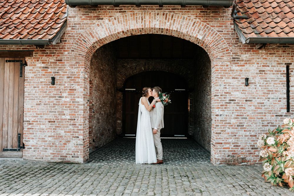 A romantic moment under a rustic brick archway with terracotta roof tiles at a charming countryside venue.
