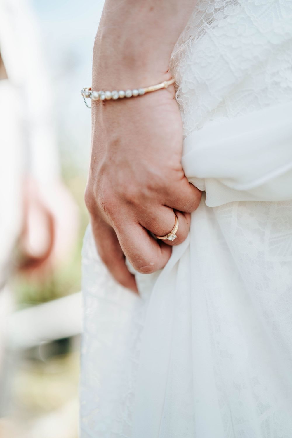 Close-up of a bride's hand wearing a pearl bracelet and wedding ring against white wedding dress fabric.
