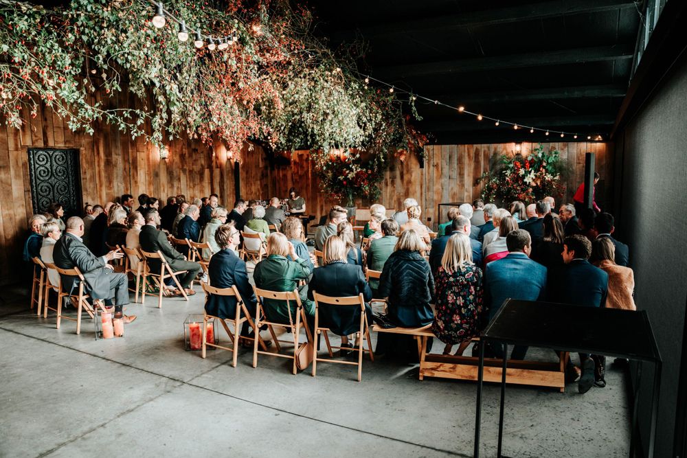 Wedding guests seated beneath enchanting floral decorations and string lights at an indoor-outdoor venue during evening ceremony.