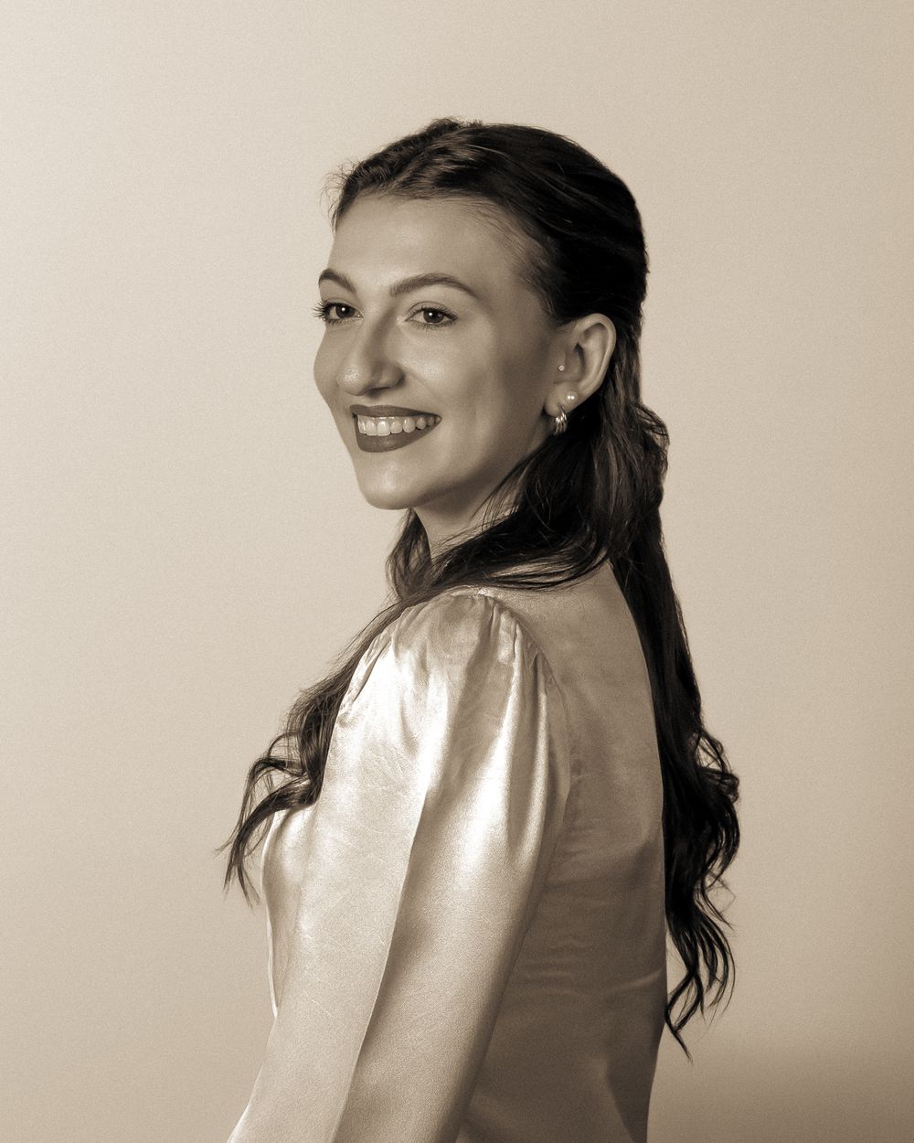 Portrait in sepia tones featuring someone in a metallic top with a warm smile.