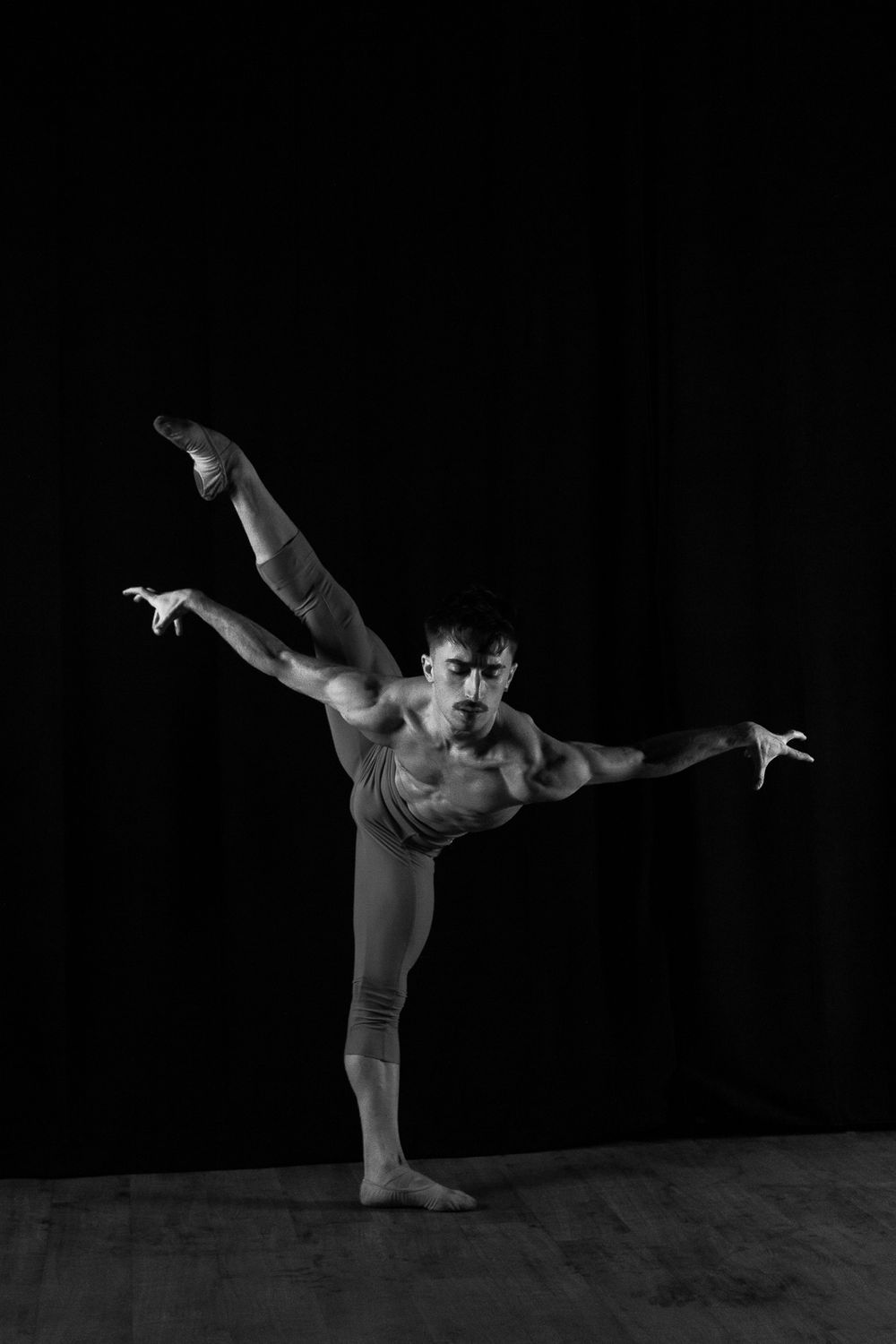 Black and white photo of a dancer performing an arabesque pose on stage.