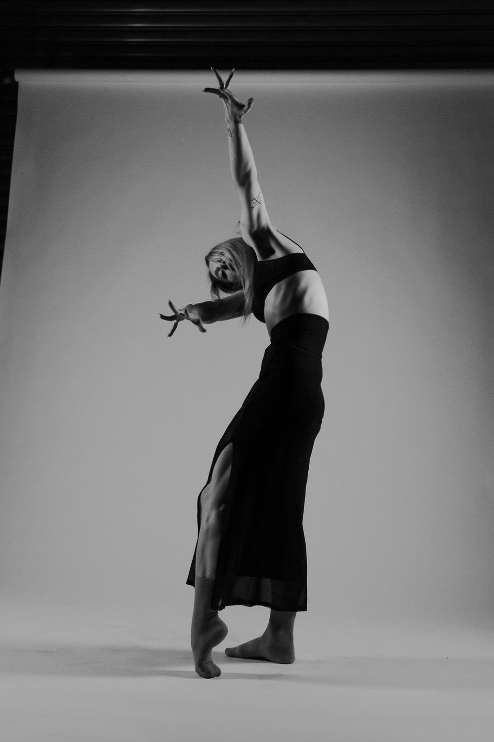 A dramatic black and white photo of a dancer in a flowing dress arching backwards with outstretched arms.