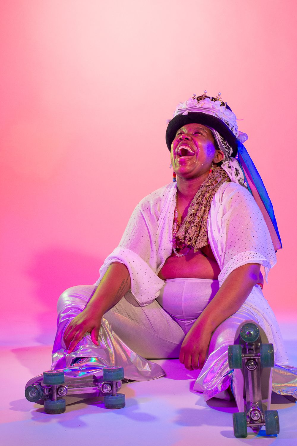 Playful portrait with roller skates and crown against pink background in studio setting.