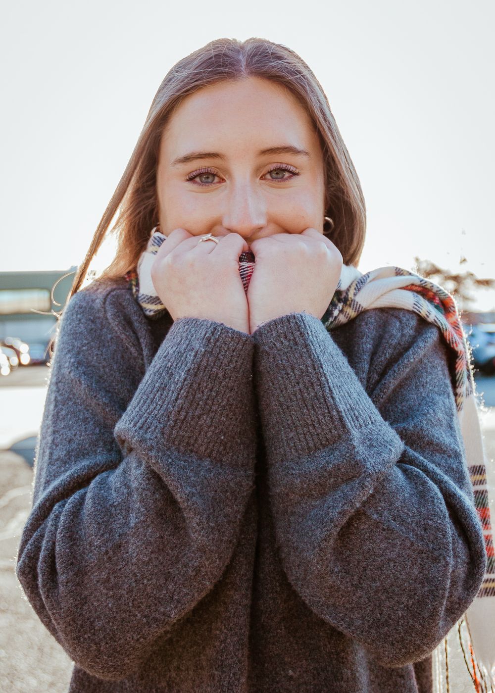 Person wearing cozy gray sweater covering face with sleeves in outdoor setting.