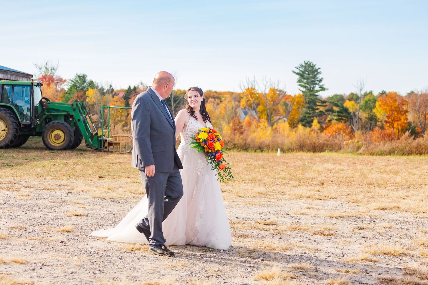 Couple walking outdoors during autumn wedding with colorful fall foliage in background.