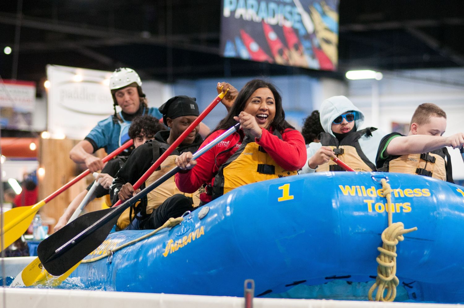 People paddling in a blue inflatable raft at an indoor rafting attraction.