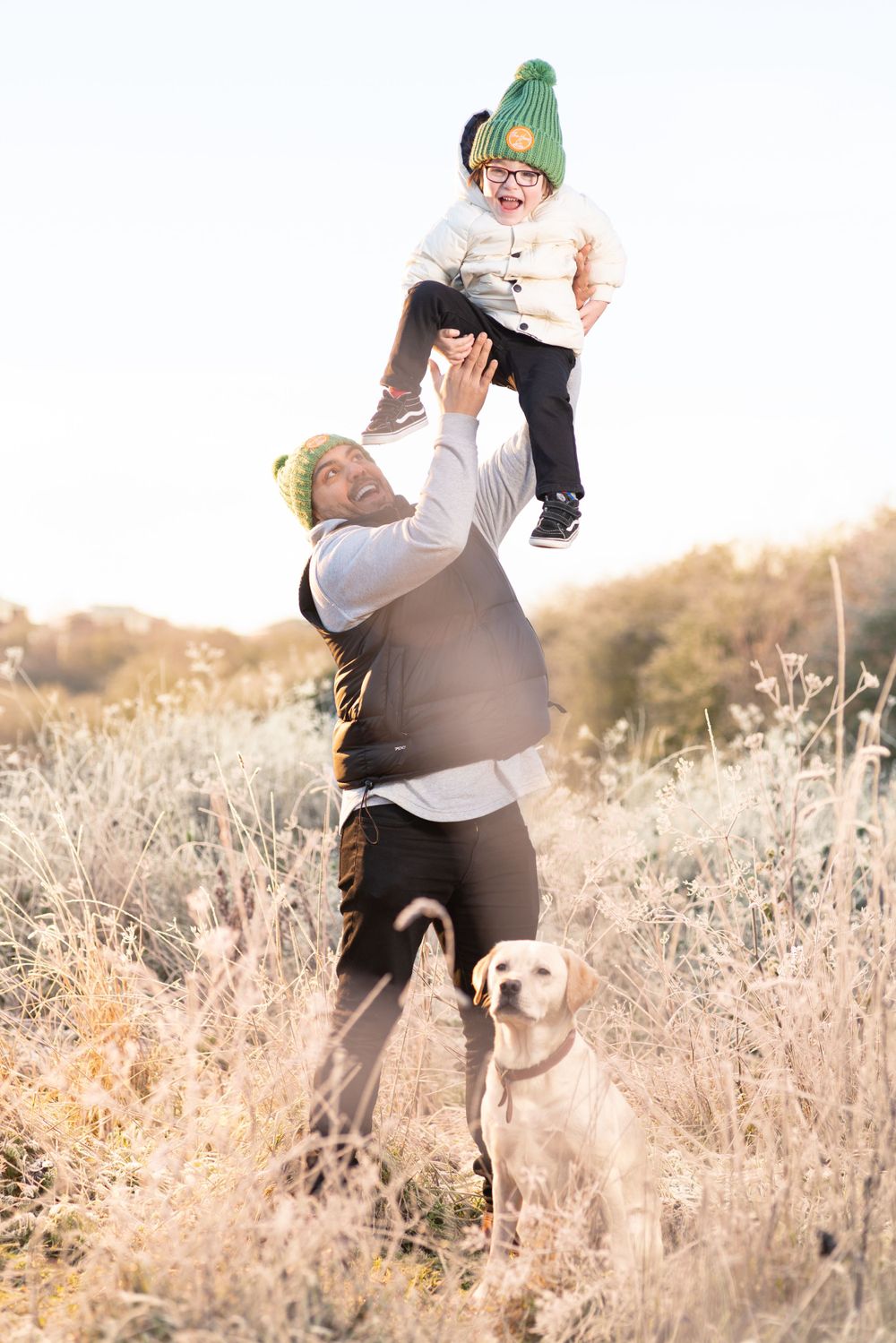 A playful family moment outdoors with a yellow lab watching nearby in a winter field.