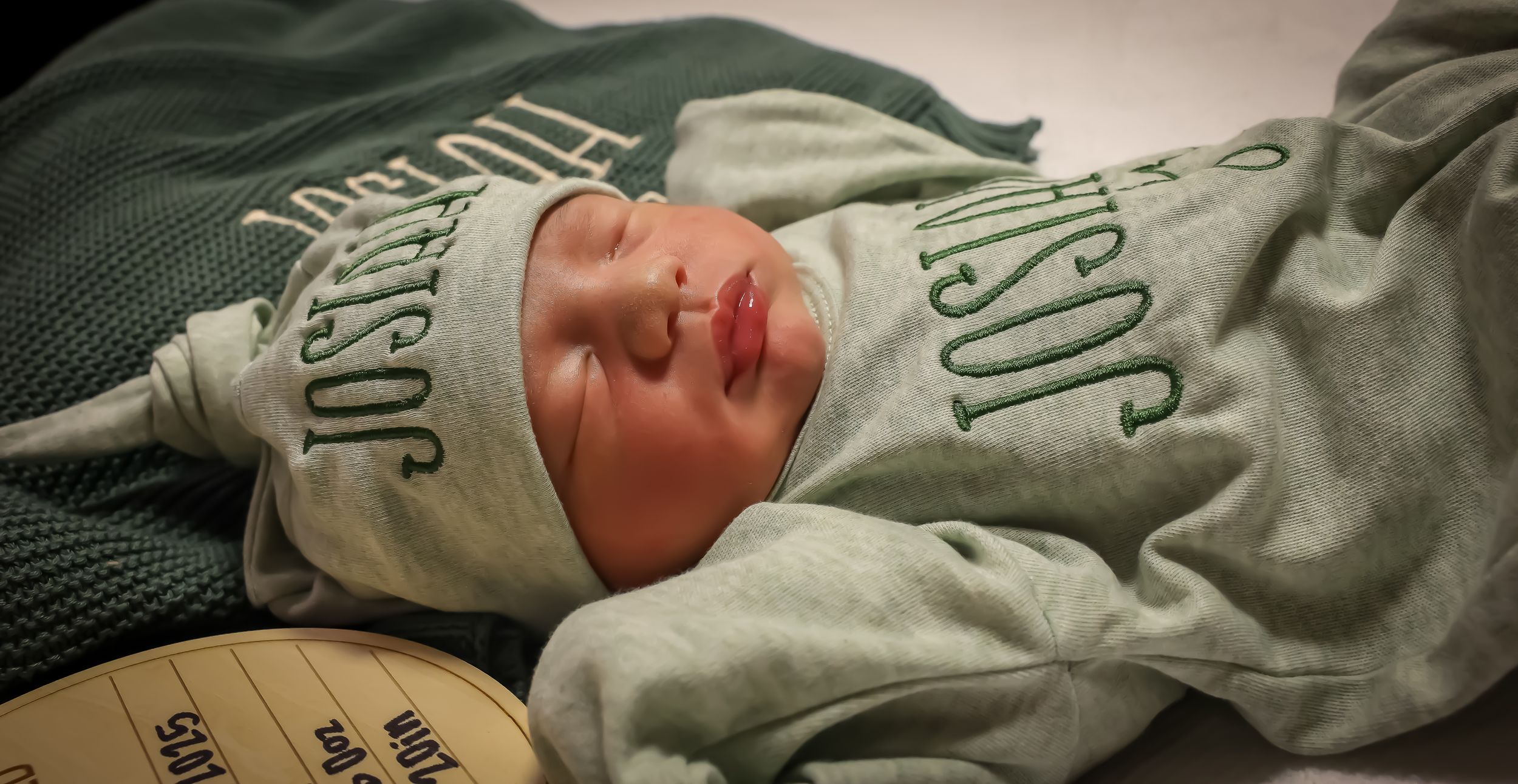 Close-up detail of sleeping newborn wearing sage green outfit.